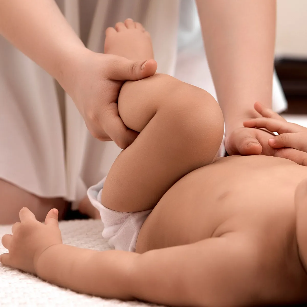 Eine Hand umfasst behutsam das angewinkelte Bein eines Babys, das auf einer hellen Decke liegt