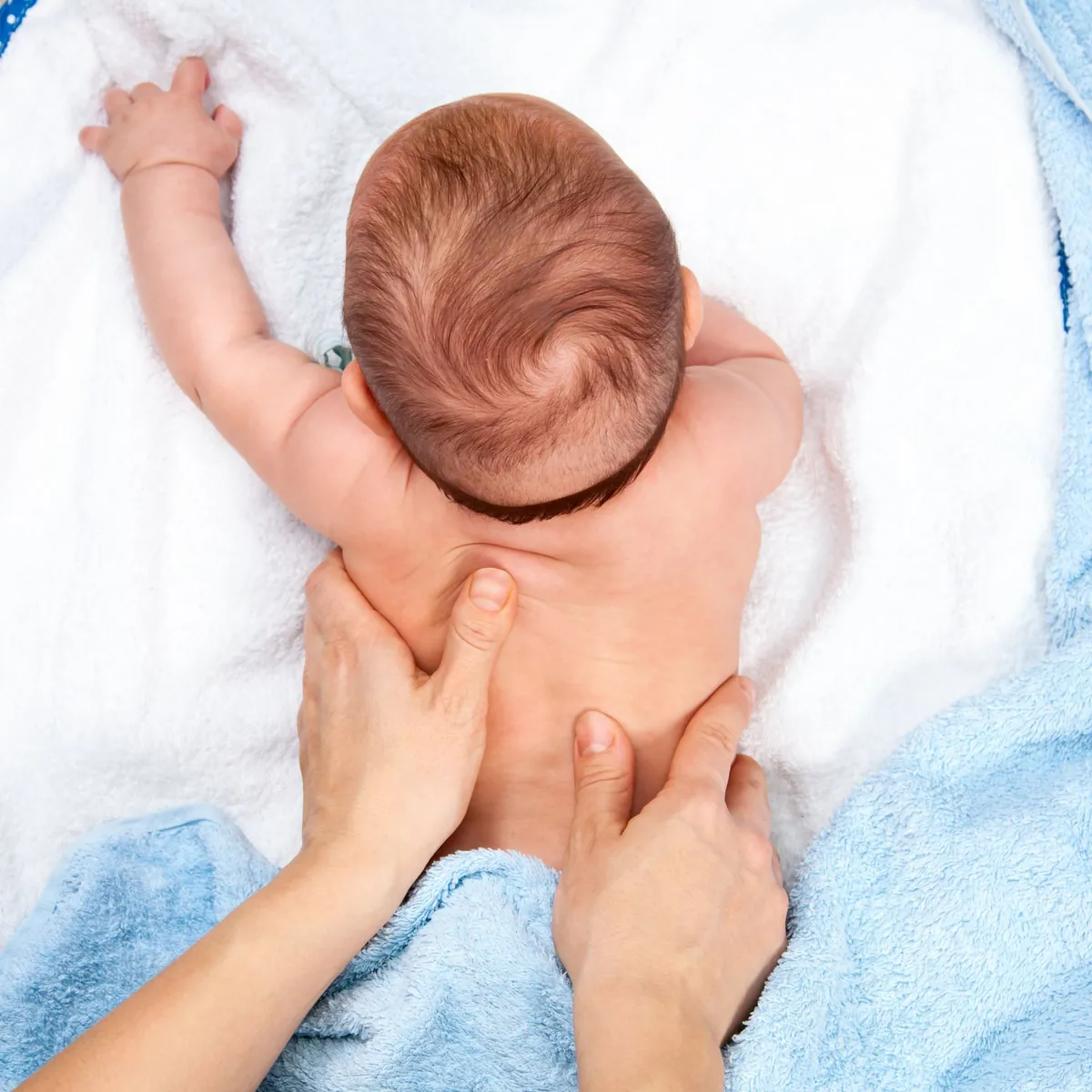 Ein Baby liegt von oben gesehen auf dem Bauch auf einem weichen Handtuch, zwei Hände streichen über seinen Rücken