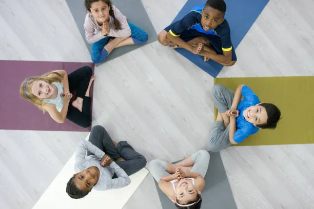 Sechs Kinder sitzen im Kreis auf bunten Matten und halten die Hände vor der Brust zusammen