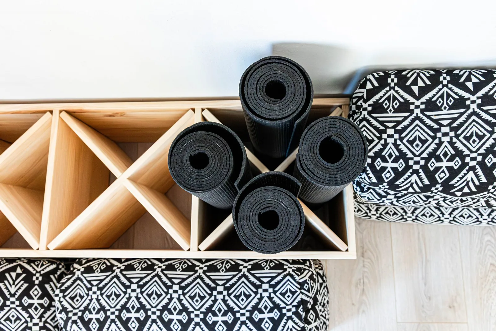 Aufgerollte Yogamatten in einem Holzregal neben gemusterten Sitzkissen