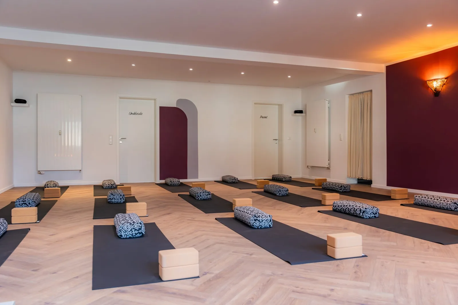 Heller Yogaraum mit Fischgrätboden, vorbereiteten Matten und Türen zu Umkleide und Praxis