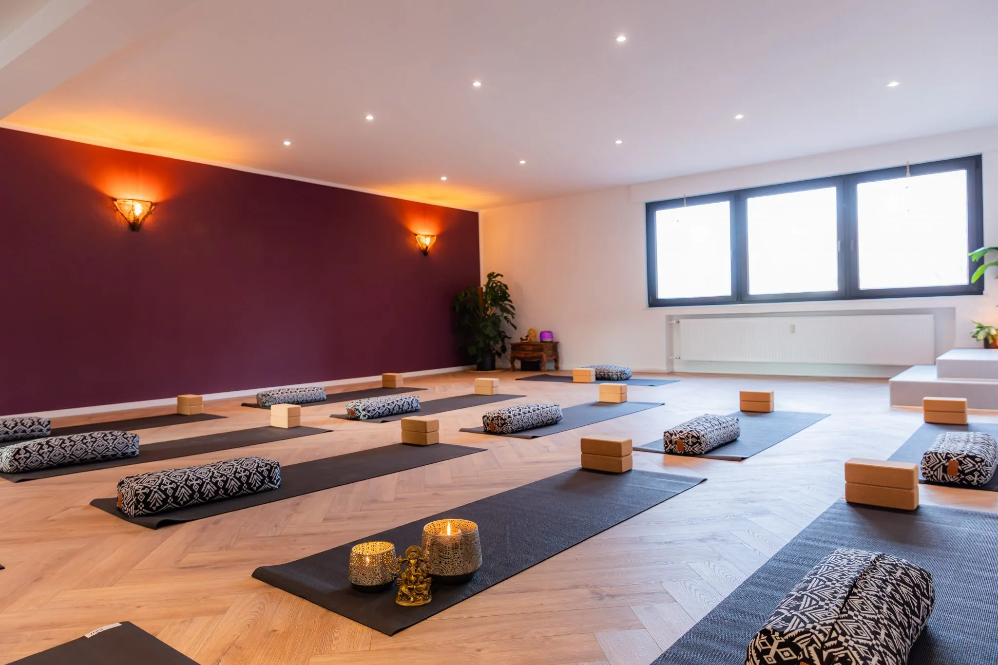 Yogaraum in Pulheim mit ausgelegten Matten, Bolstern und Korkblöcken vor einer beerenroten Wand
